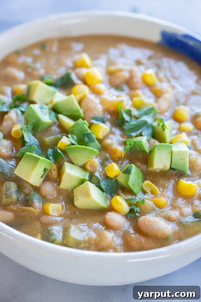 Summer Garden Zucchini White Bean Chili 6 A close-up view of a bowl of creamy vegan white bean chili, richly textured with visible pieces of zucchini and corn, invitingly garnished with fresh herbs.