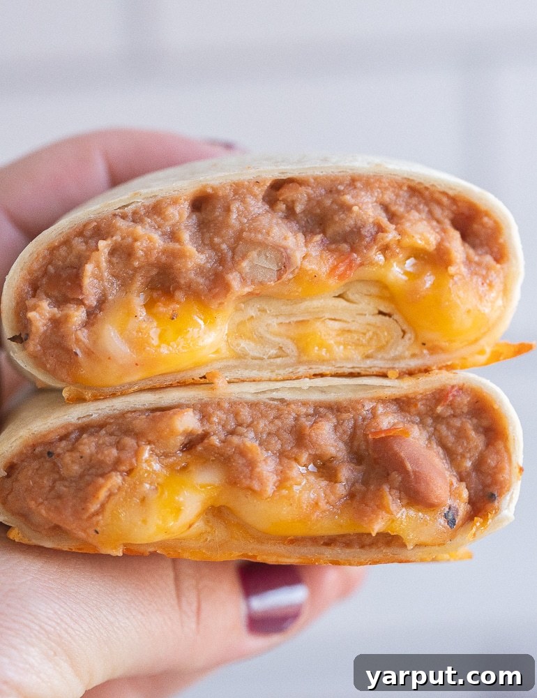 close up of a hand holding a bean and cheese burrito that has been cut in half, showcasing the gooey cheese and savory beans inside