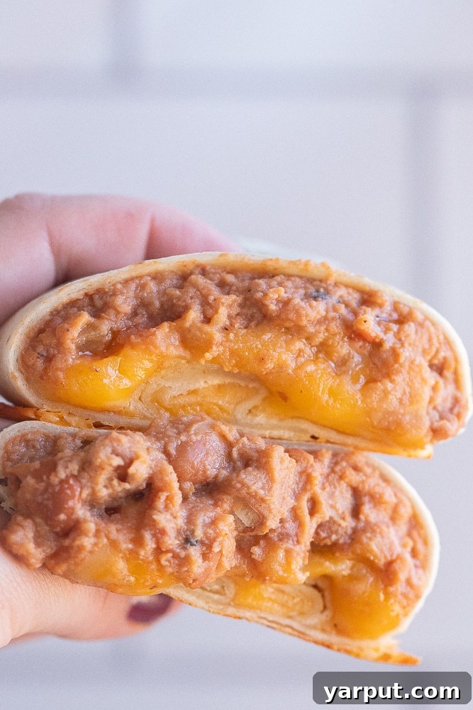 close up of a hand holding a bean and cheese burrito that has been cut in half, showing the rich filling and golden tortilla