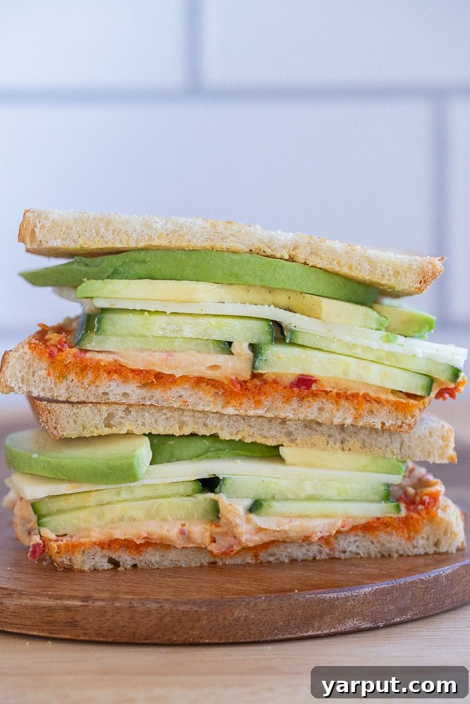 A beautifully presented hummus and avocado sandwich, cut in half and stacked atop each other, ready to eat.