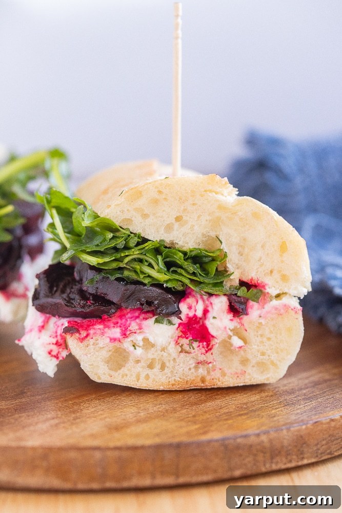 Vibrant Roasted Beet and Zesty Goat Cheese Sandwiches 6 close up of a roasted beet sandwich cut in half, showcasing layers of beet, cheese, and arugula