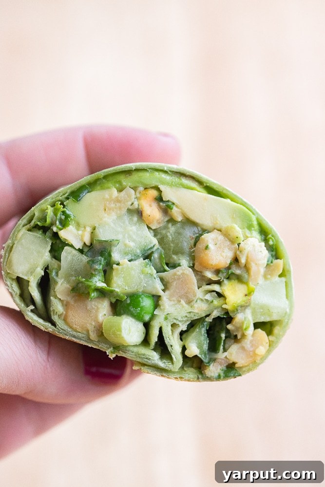 Emerald Goddess Chickpea Rolls 7 a close-up of a perfectly halved vegan green goddess chickpea wrap, held delicately by a hand, showcasing its vibrant layers
