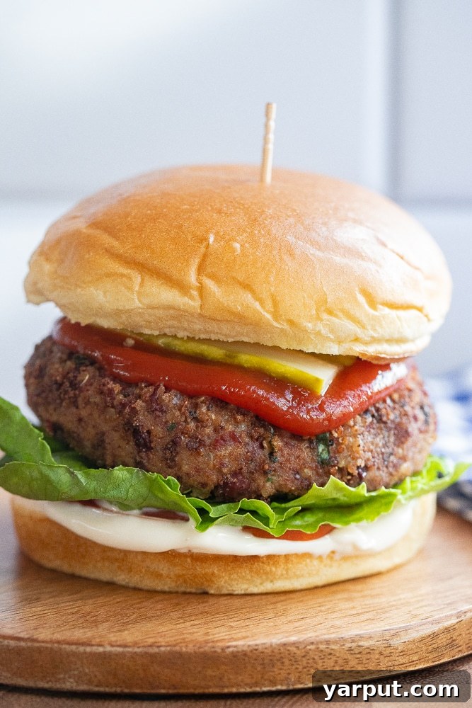 Close-up of a high-protein kidney bean burger loaded with fresh tomato slices, crisp lettuce, and tangy pickles on a toasted bun.