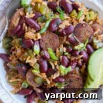 A bowl of vegetarian red beans and rice, topped with fresh green onions and sliced avocado.