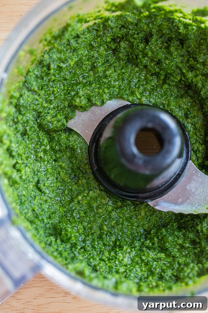 Zesty Kale Pesto 5 Vibrant green kale pesto being processed in a food processor, showing the texture as olive oil is slowly drizzled in.