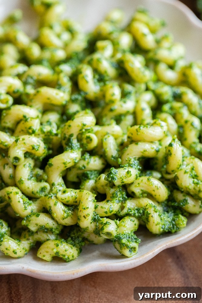 Zesty Kale Pesto 7 A plate of perfectly tossed pesto pasta, featuring vibrant green kale pesto, fresh cherry tomatoes, and basil leaves, ready to be enjoyed.