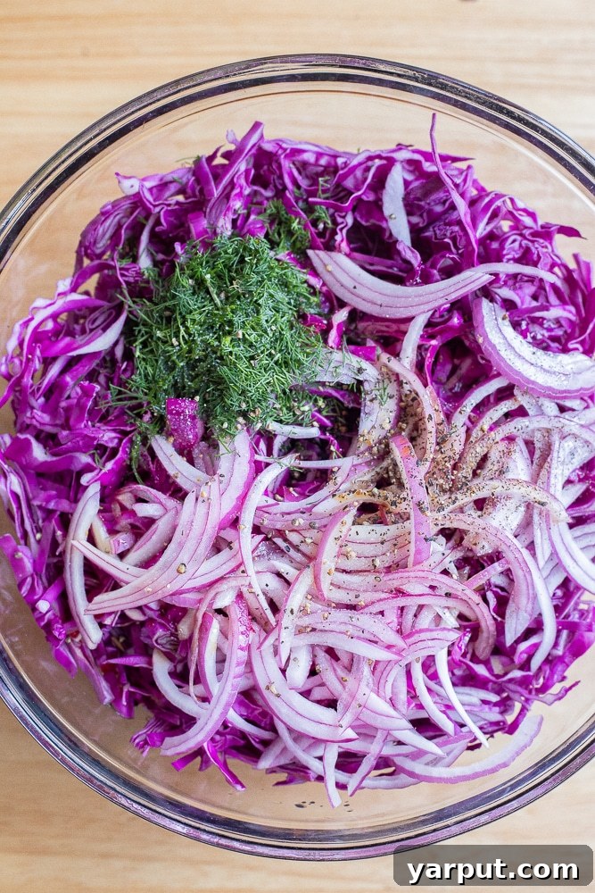 Freshly sliced purple cabbage, red onion, and dill, showcasing the raw ingredients for the salad.