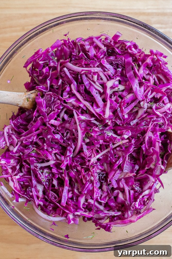 Hands mixing the vibrant purple cabbage salad in a large bowl, showing the ingredients coming together.
