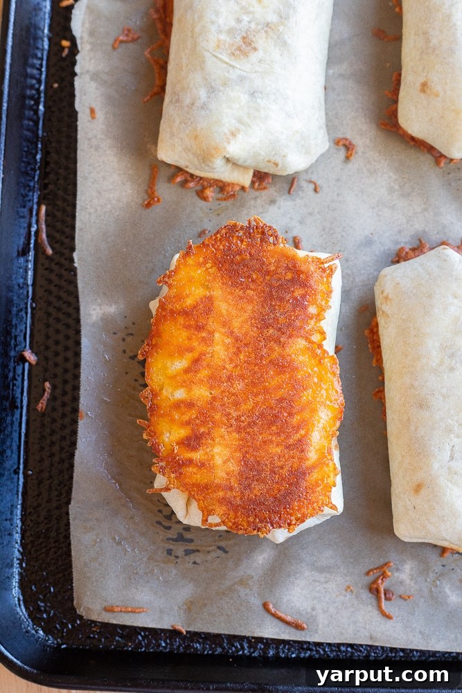 Three perfectly baked vegetarian bean and rice burritos stacked neatly, showcasing their golden-brown tortillas and crispy cheese on the bottom.