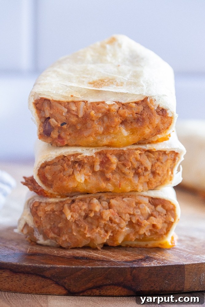 A close-up of three vegetarian bean burritos stacked on top of each other, ready to be served.