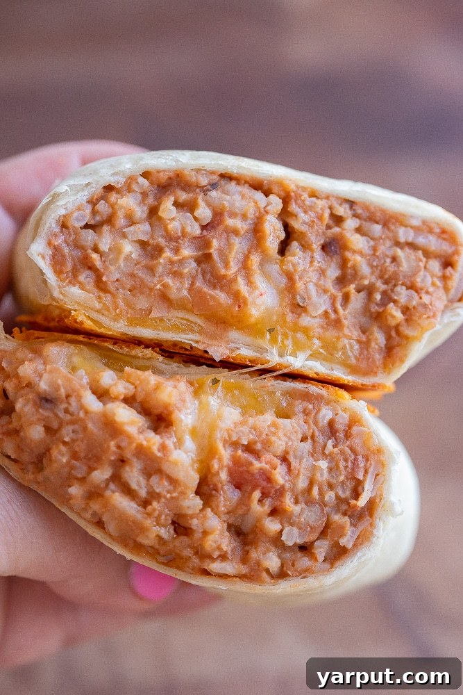 A close-up of a hand holding a vegetarian bean burrito that has been sliced in half, showcasing the hearty filling.