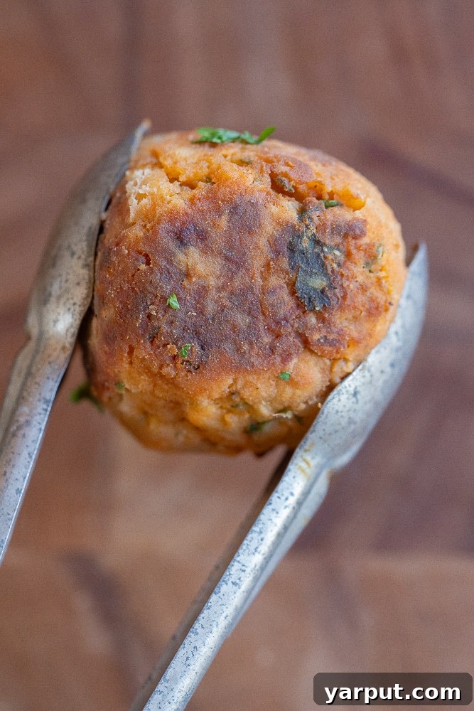 Effortless Veggie Meatballs 7 Close-up of a perfectly crispy and browned vegetarian meatball, held delicately by a pair of tongs, highlighting its enticing texture.