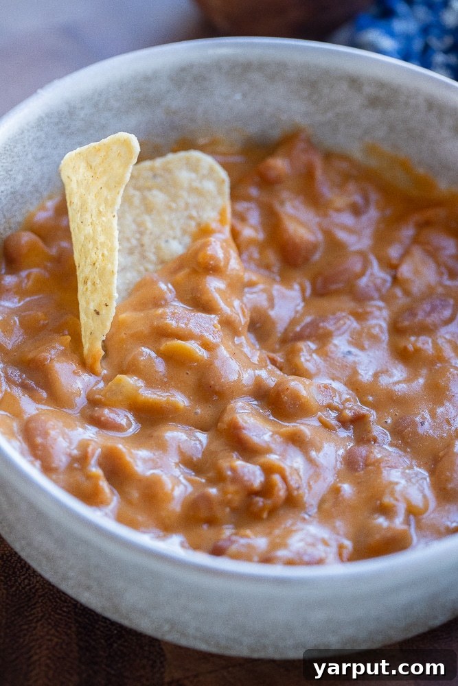 A close-up of cheesy beans in a bowl with a tortilla chip dipped in, showcasing the creamy texture.
