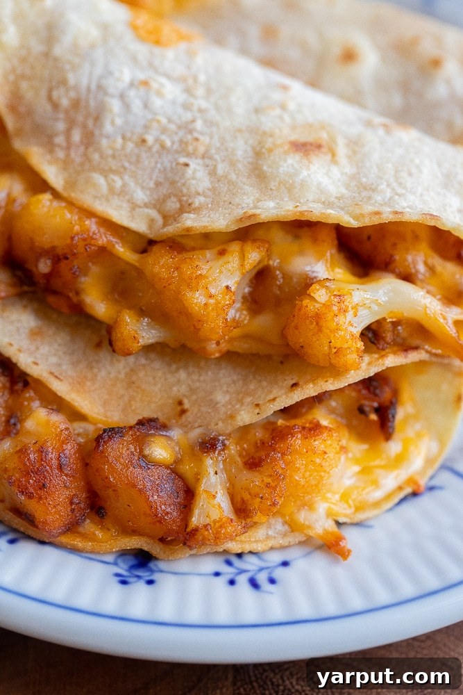 Two crispy cauliflower and potato tacos filled with seasoned vegetables, cheese, and fresh toppings.