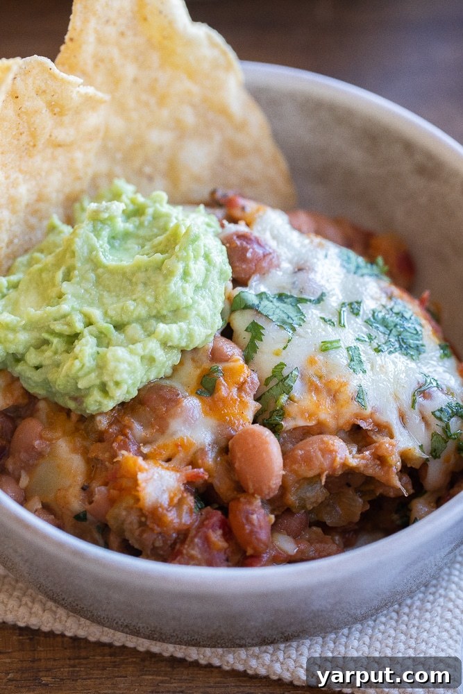 A skillet of bubbling cheesy green chile pinto beans, ready to be served.