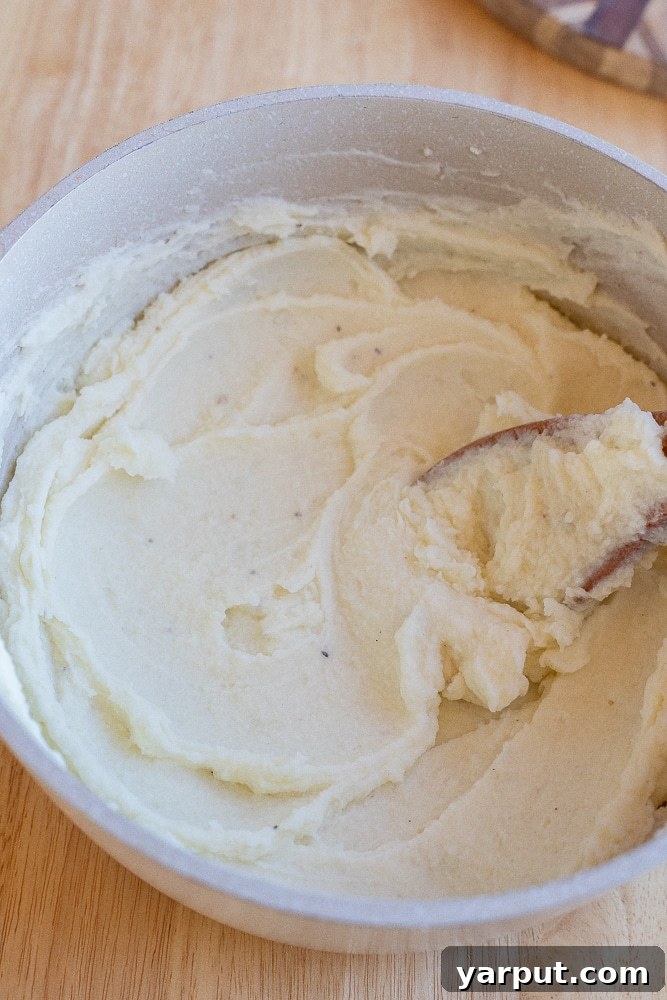 Velvety Smooth Mashed Potatoes 5 The process of mashing potatoes with a potato ricer, showing the smooth texture being produced.