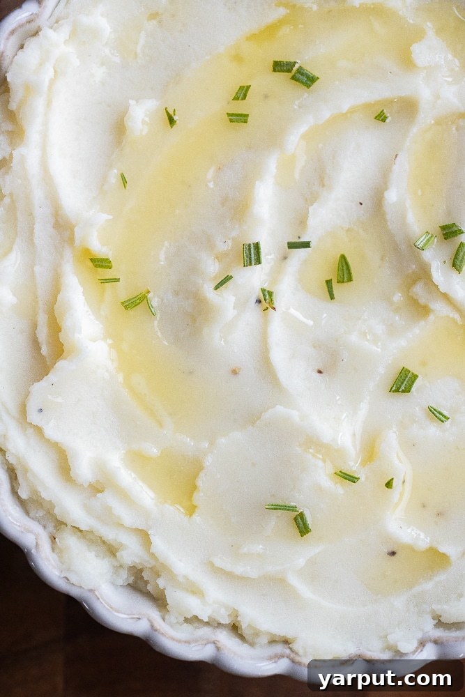 Velvety Smooth Mashed Potatoes 6 A bowl of creamy mashed potatoes with a serving spoon, garnished with green onions, ready to be served.