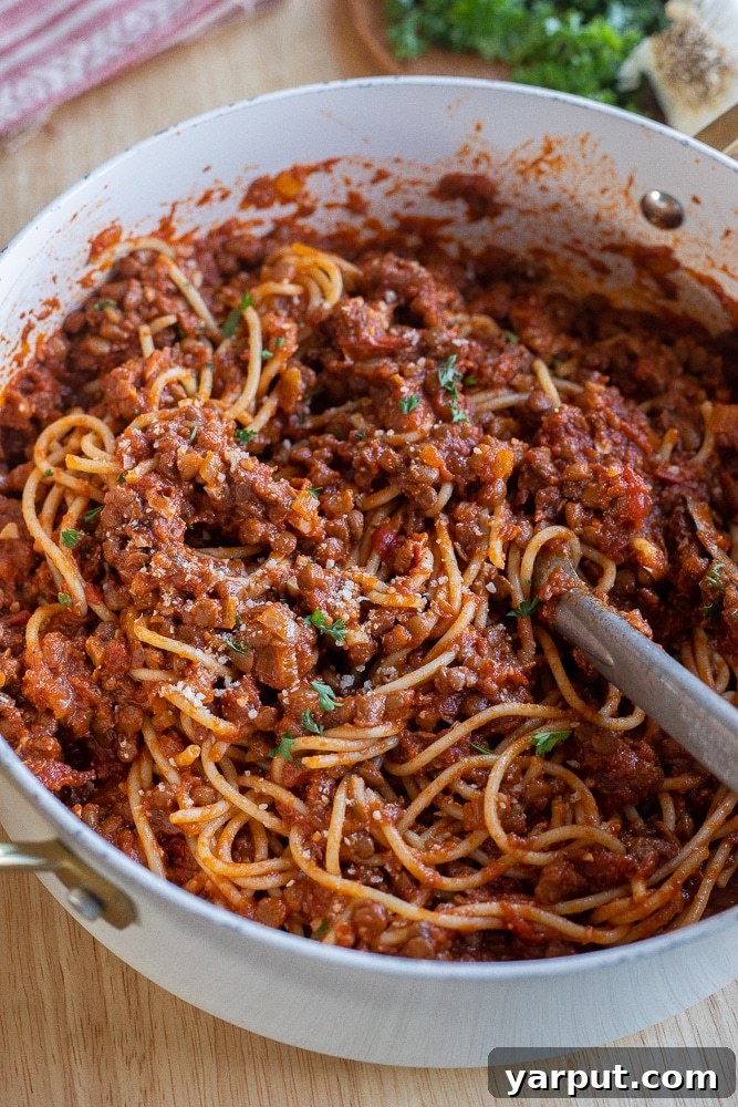 A large saucepan overflowing with perfectly cooked spaghetti generously coated in a rich meaty lentil sauce, topped with grated Parmesan and fresh parsley.