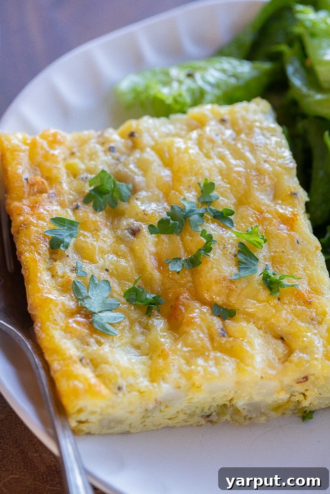 Baked Eggs with White Cheddar, Leeks, and Cauliflower 6 A perfectly golden slice of vegetarian cauliflower leek egg bake, showing the vibrant cauliflower and leek pieces embedded within the fluffy egg and melted white cheddar cheese, served on a pristine white plate.