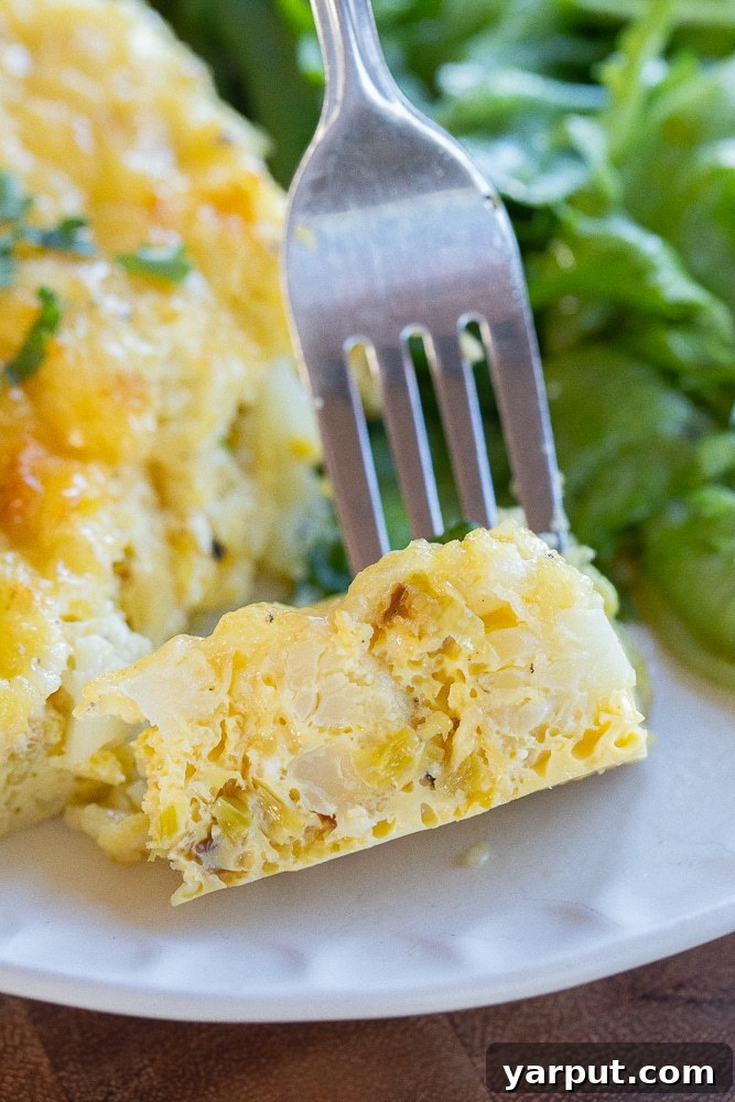 Baked Eggs with White Cheddar, Leeks, and Cauliflower 8 A tempting close-up of a single slice of Cauliflower Leek and White Cheddar Egg Bake, showing the rich, fluffy texture of the eggs, the tender pieces of cauliflower and leek, and the beautifully melted white cheddar cheese on top.