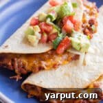 Two cheesy baked lentil tacos on a plate with fresh tomato topping.