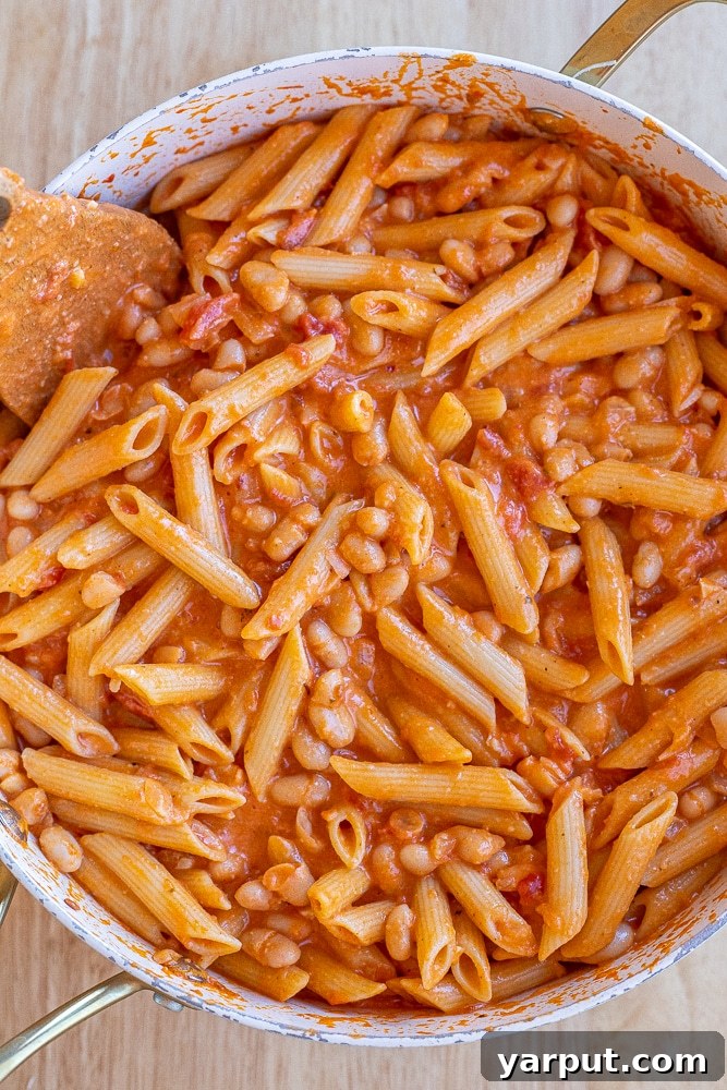 large pan full of vibrant creamy tomato and white bean pasta, ready to be served