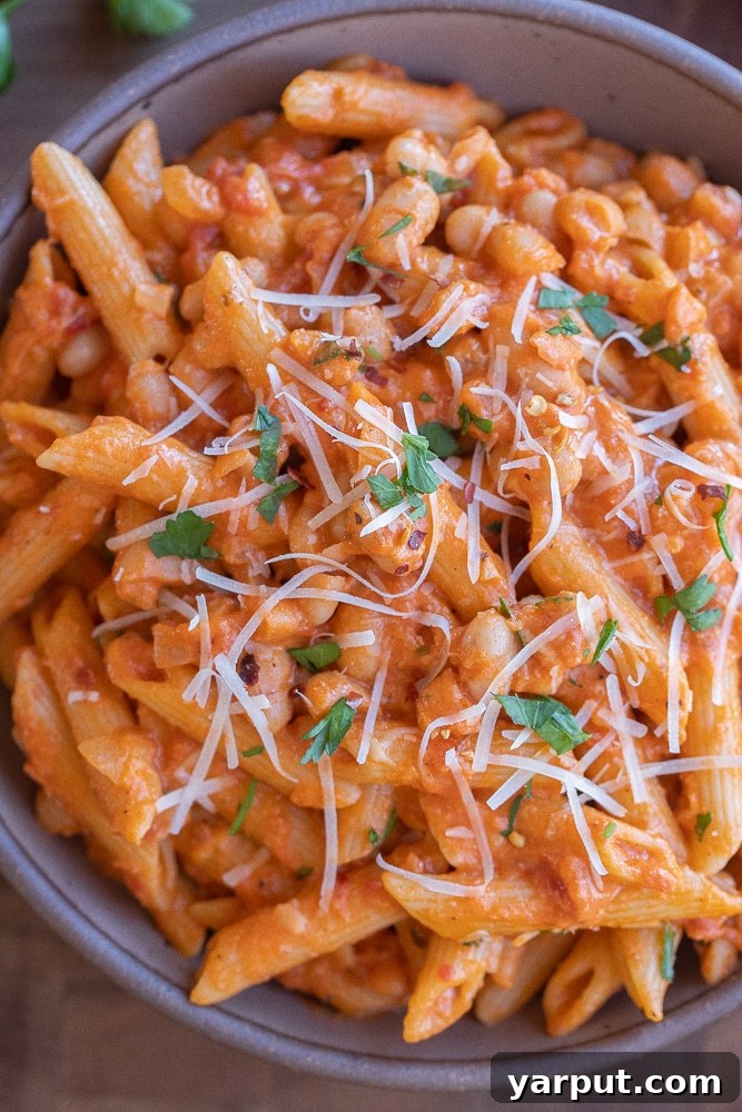 close up of a bowl of creamy tomato pasta with white beans, garnished with fresh herbs