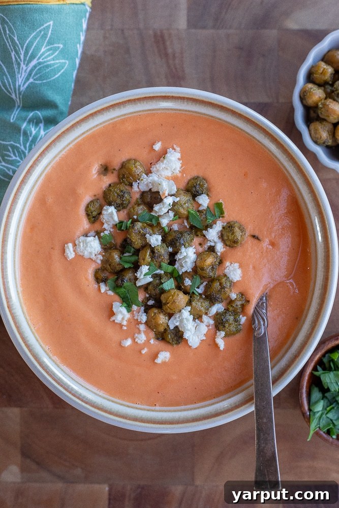A close-up shot of a cozy bowl of creamy roasted tomato feta soup, adorned with golden crispy pesto chickpeas and a sprinkle of fresh feta crumbles, ready to be enjoyed.