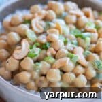 A vibrant bowl of Green Curry Chickpeas, garnished with fresh herbs and cashews.
