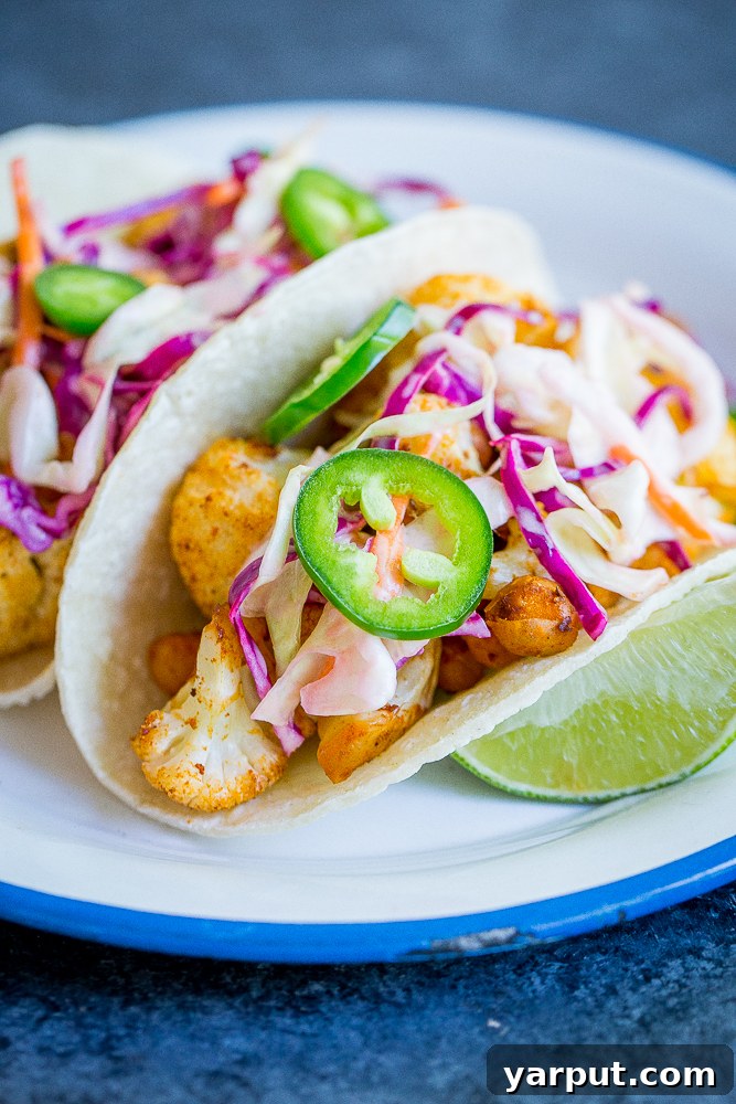Close-up of fully loaded BBQ Cauliflower and Chickpea Tacos, showcasing the rich BBQ coating and fresh creamy lime slaw.