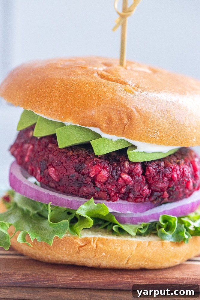 Close-up of a delectable vegan beet burger in a bun, adorned with creamy avocado slices, ready to be enjoyed.
