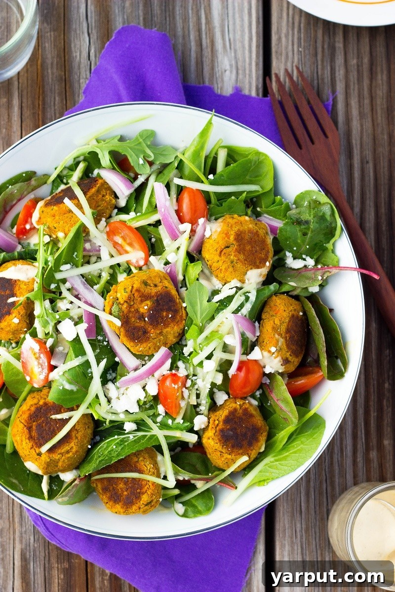 A vibrant bowl of Roasted Carrot Falafel Salad with a generous drizzle of Citrus Tahini Dressing, garnished with feta cheese, red onion, and cherry tomatoes, invitingly presented.