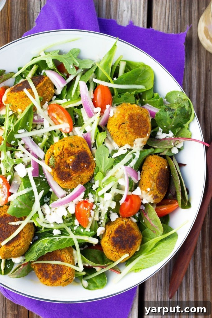 A close-up of the fully assembled Roasted Carrot Falafel Salad, featuring rich feta, sliced red onions, vibrant cherry tomatoes, and tender falafel, all dressed to perfection.