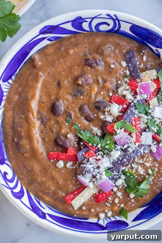 close up of easy black bean soup in a bowl with avocado, cilantro, and tortilla strips
