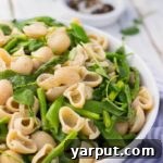 A vibrant Spring Pasta Salad, showcasing fresh pasta, asparagus, watercress, and sugar snap peas, topped with a light dressing.