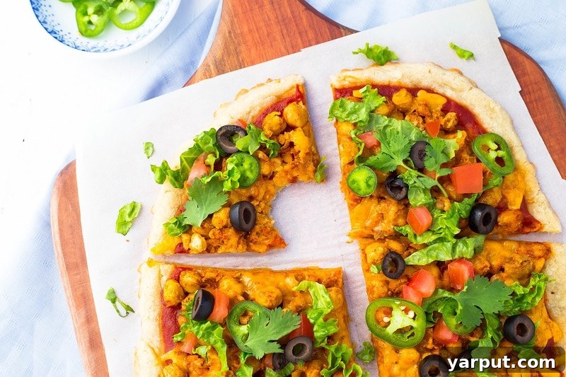 Fiesta Smashed Chickpea Pizza 4 A hand gently mashing cooked chickpeas in a bowl with a potato masher, illustrating the preparation of the taco pizza topping.