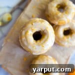 A stack of freshly baked gluten-free pumpkin donuts, glazed with a sweet orange icing, ready to be served. Ideal for fall breakfasts and desserts.