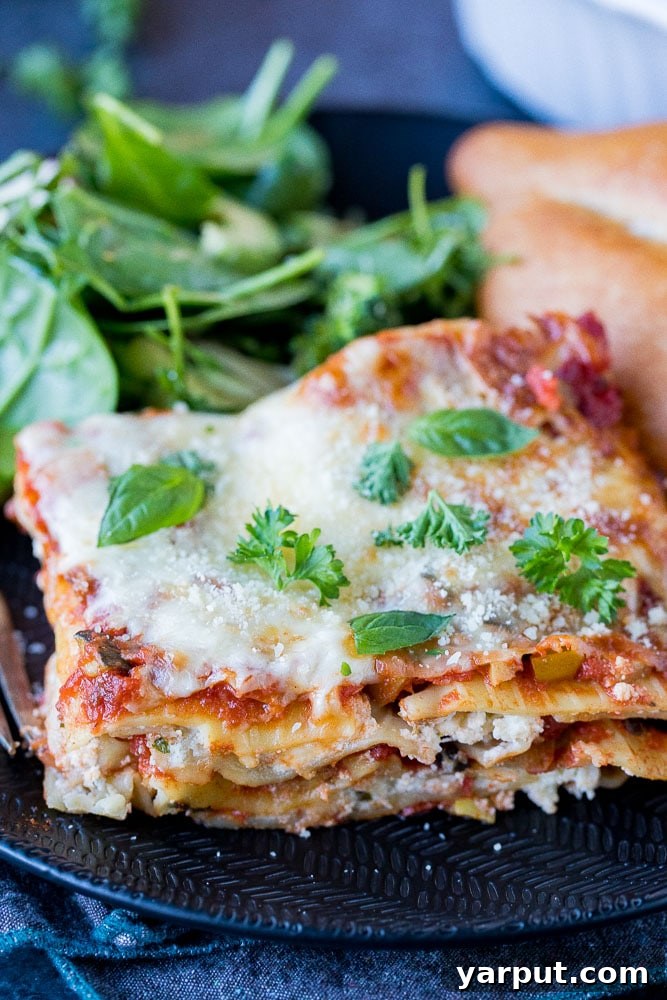 Perfect Plant-Based Lasagna 2 A generous slice of homemade vegetarian lasagna, layered with roasted vegetables, ricotta, and mozzarella, served on a white plate alongside a fresh green salad and crusty garlic bread.