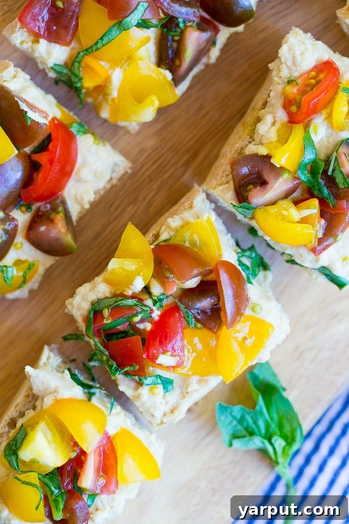 Roasted Garlic Hummus Toasts 5 A side view of a stack of Roasted Garlic Hummus Bruschetta, showcasing the distinct layers of toasted bread, creamy hummus, and the colorful tomato topping, ready to be enjoyed as a refreshing snack.