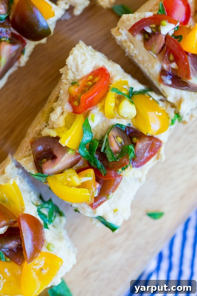 Roasted Garlic Hummus Toasts 6 A top-down view of several pieces of Roasted Garlic Hummus Bruschetta arranged on a plate, highlighting the fresh, bright colors of the cherry tomatoes and basil against the creamy hummus and golden bread, perfect for sharing.