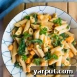 Creamy White Bean Pasta with Sweet Potato & Kale in a pot with serving spoon.
