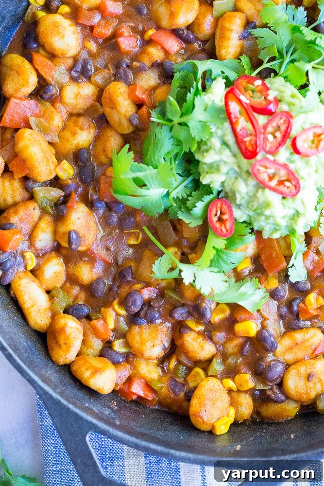 A close-up shot of the finished Gnocchi Enchilada Skillet, topped with fresh avocado and cilantro, ready to be served.