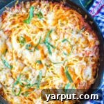 A baked zucchini noodle spaghetti dish, garnished with fresh basil, in a cast iron skillet.
