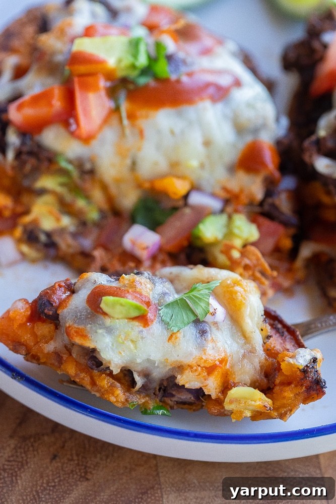 Hearty Black Bean Sweet Potato Bake 7 A close-up shot of a Black Bean Roasted Sweet Potato with a bite taken out, revealing the rich layers of cheesy beans and tender sweet potato inside, making it truly irresistible.