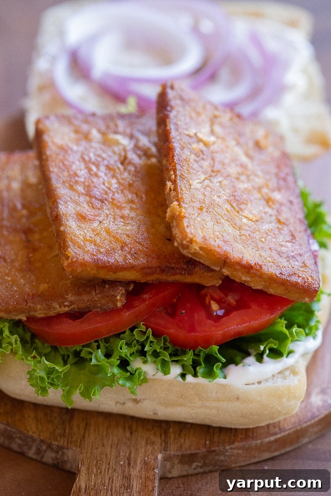 Close-up of crispy tofu bacon slices layered on a sandwich with fresh lettuce and tomatoes.