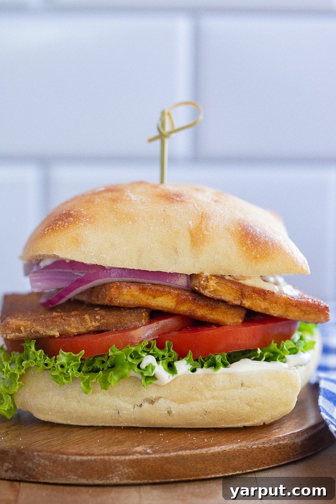 A perfectly cut vegetarian BLT sandwich on a wooden cutting board, held together with a toothpick.