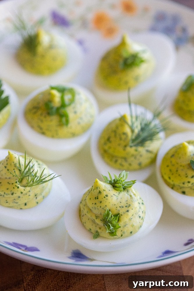 Herbal Ambrosia Deviled Eggs 2 Green Goddess Deviled Eggs arranged elegantly on a serving plate, garnished with fresh herbs and lemon wedges.