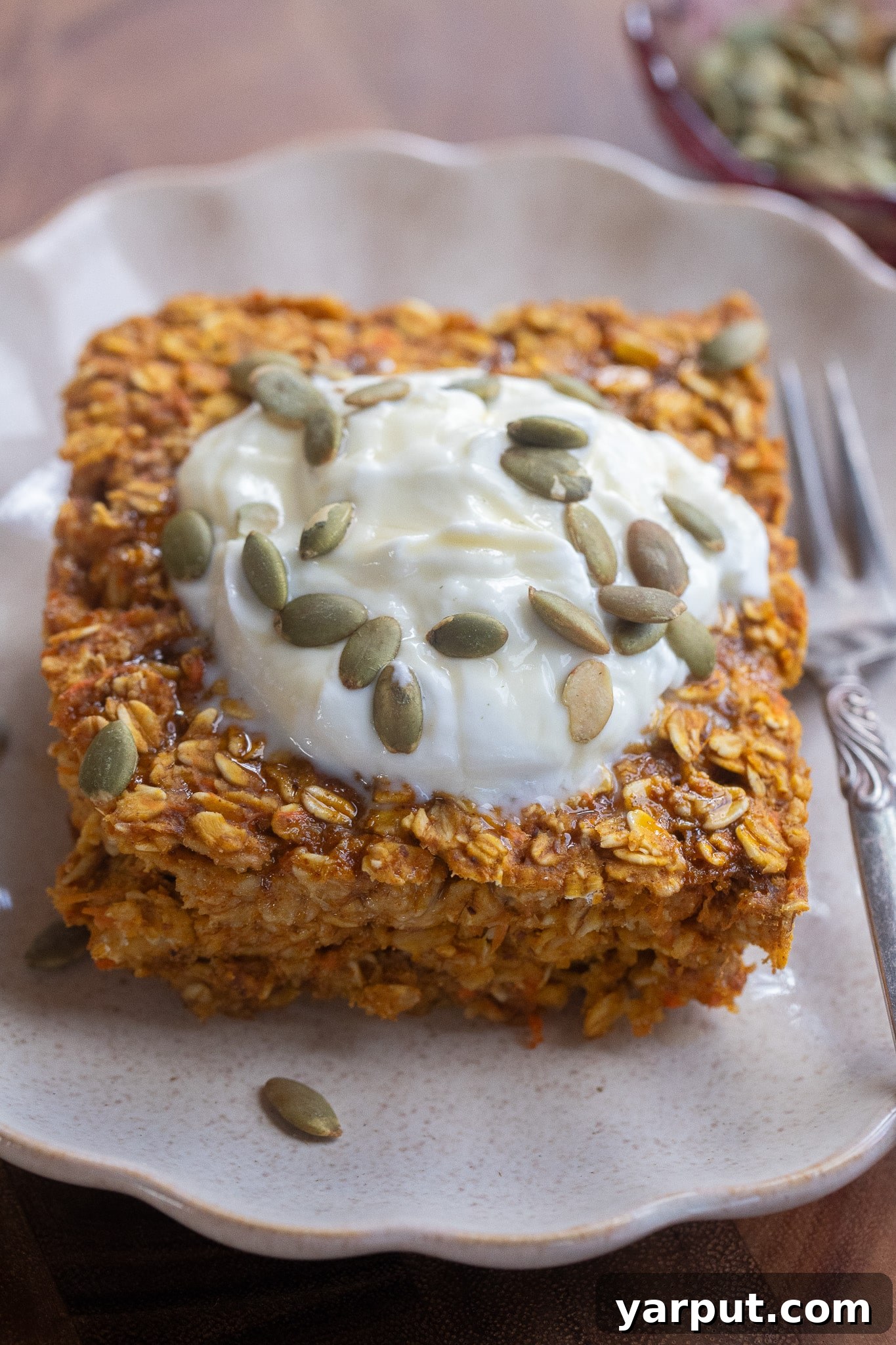 Warm Pumpkin, Ginger & Turmeric Baked Oatmeal 2 close up of a slice of pumpkin ginger turmeric baked oatmeal on a plate topped with yogurt and pumpkin seeds.
